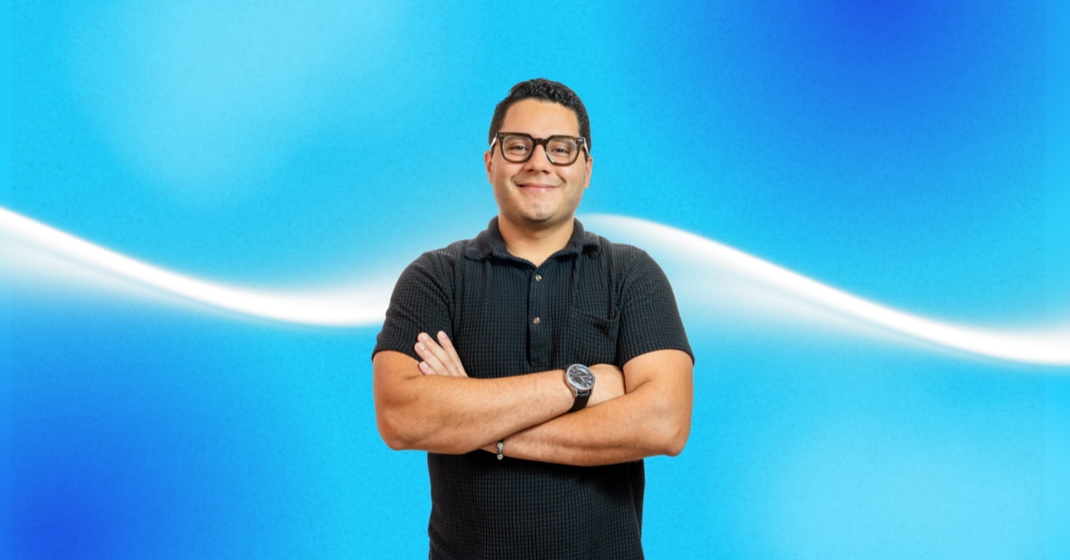 Persona en el medio de la imagen con los brazos cruzados y sonriendo, tiene lentes